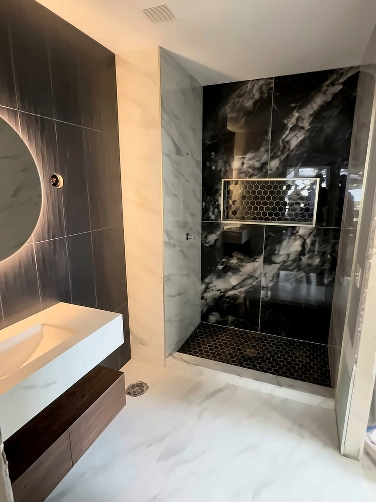 After: bathroom with black marble-look shower walls, a lit hexagon niche and hexagon mosaic shower floor