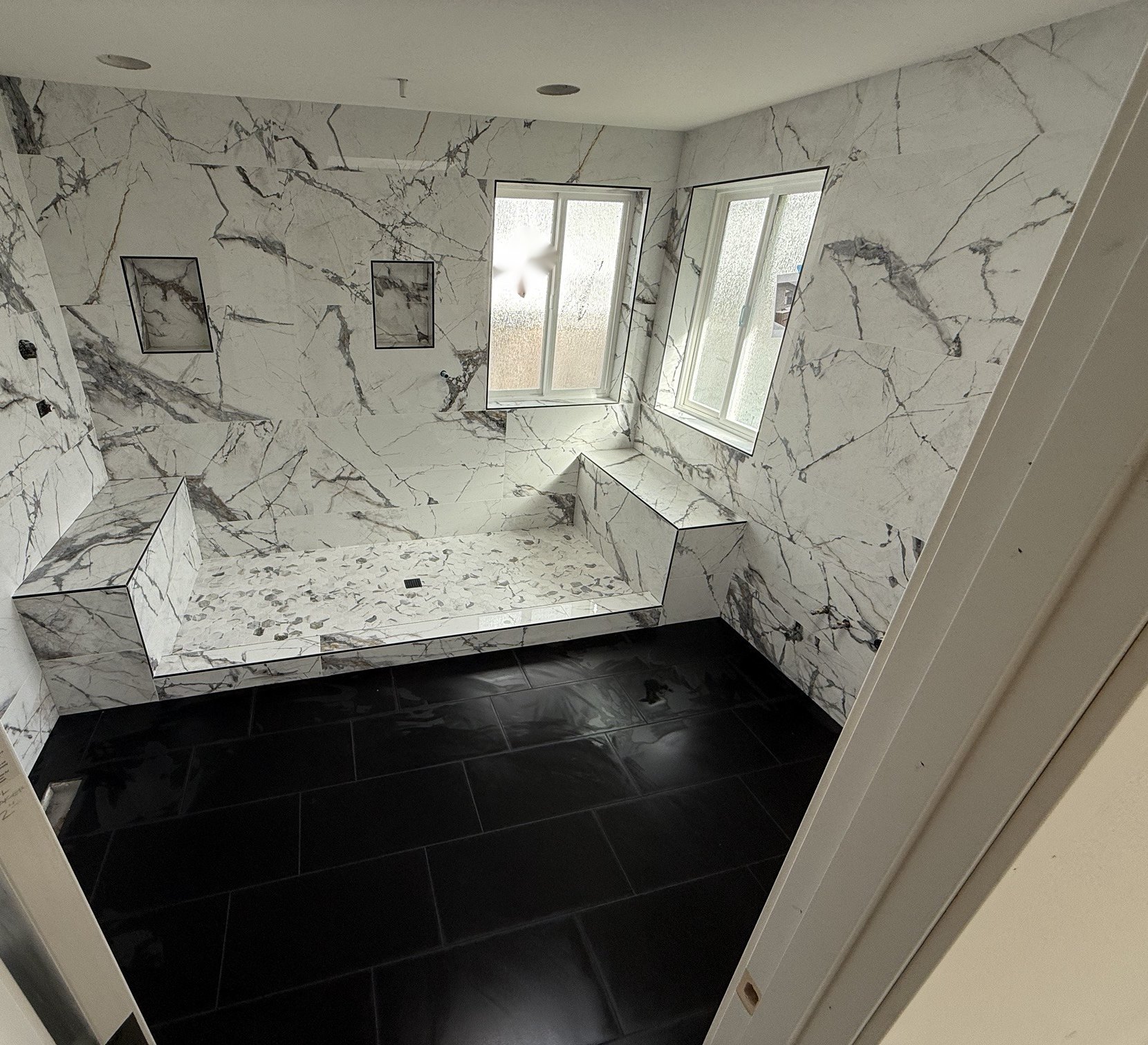 Walk-in shower with marble-look large format tile, two benches, twin niches and black tile floor