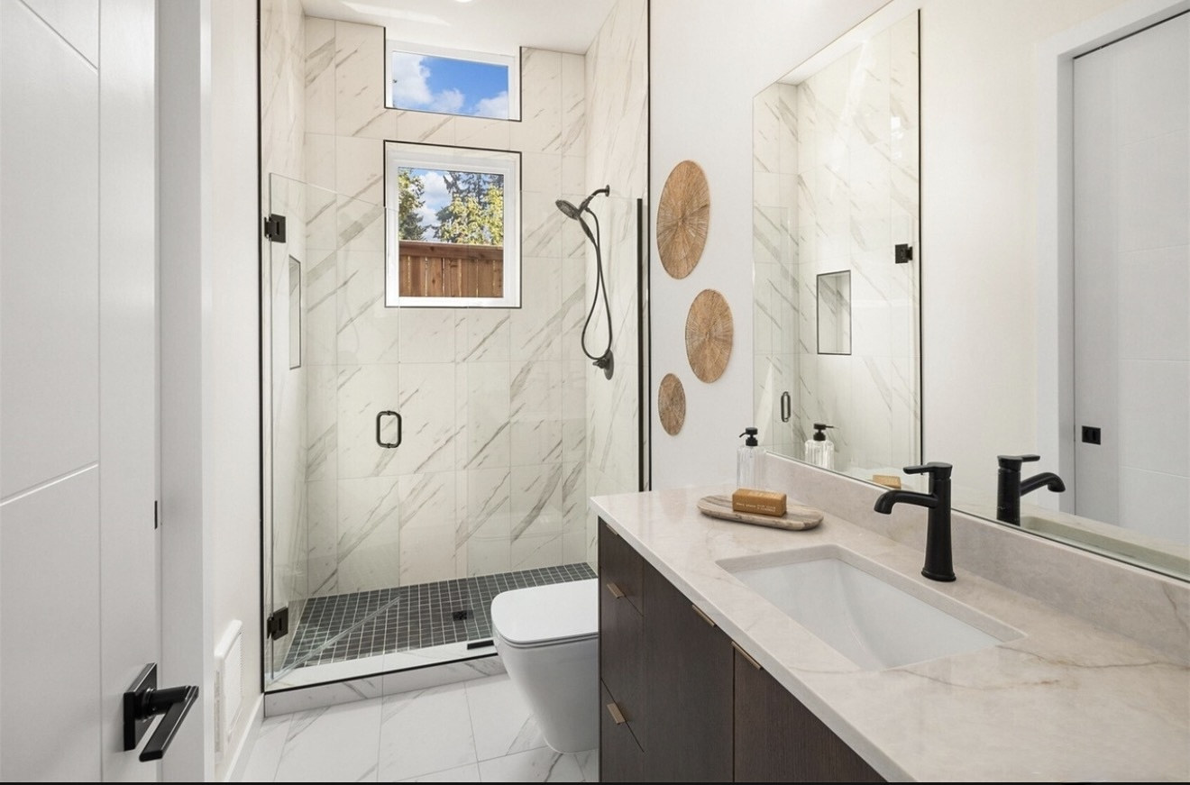 Marble tile walk-in shower with glass door and black grid floor